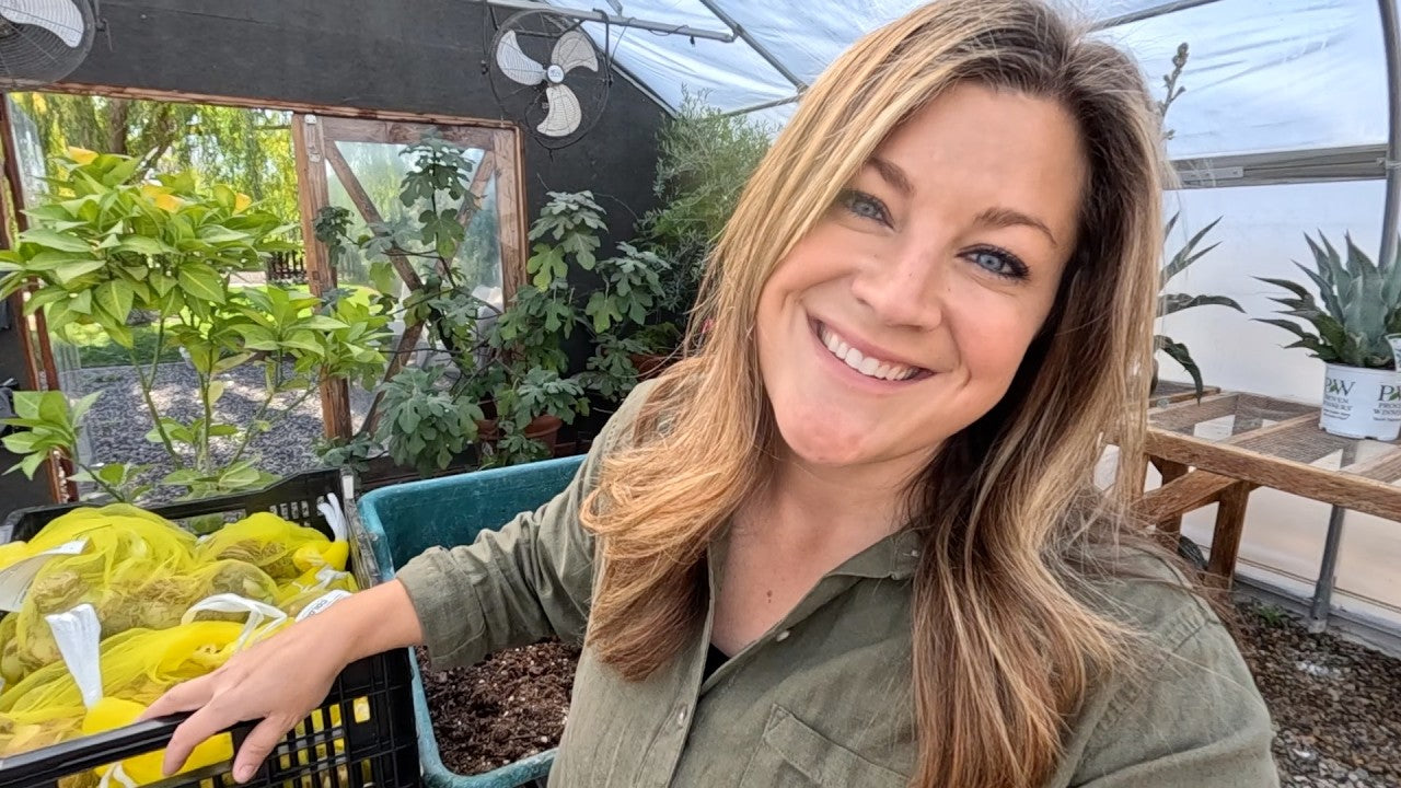 laura smiling with tools and plants inside her greenhouse 