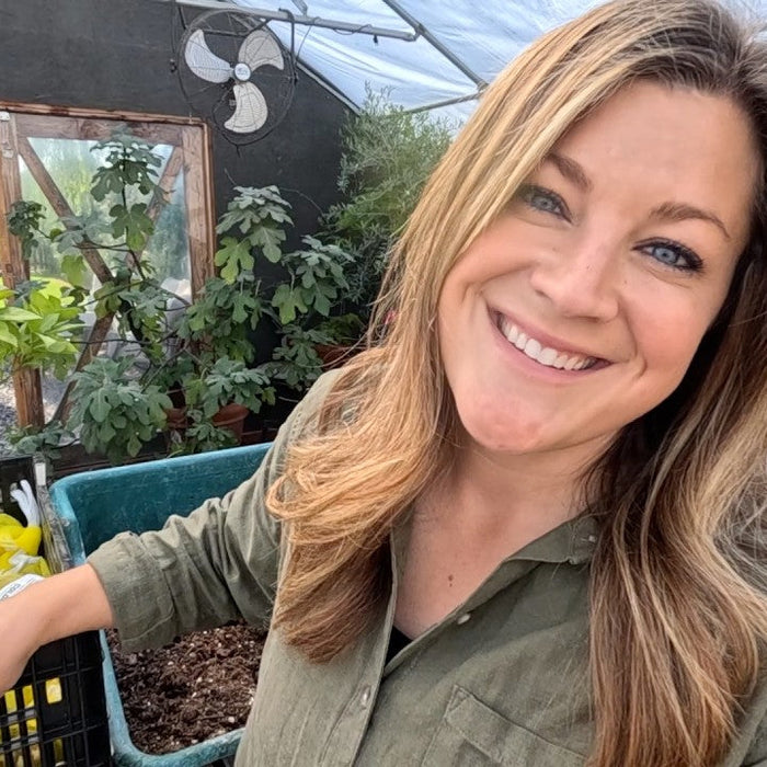 laura smiling with tools and plants inside her greenhouse 
