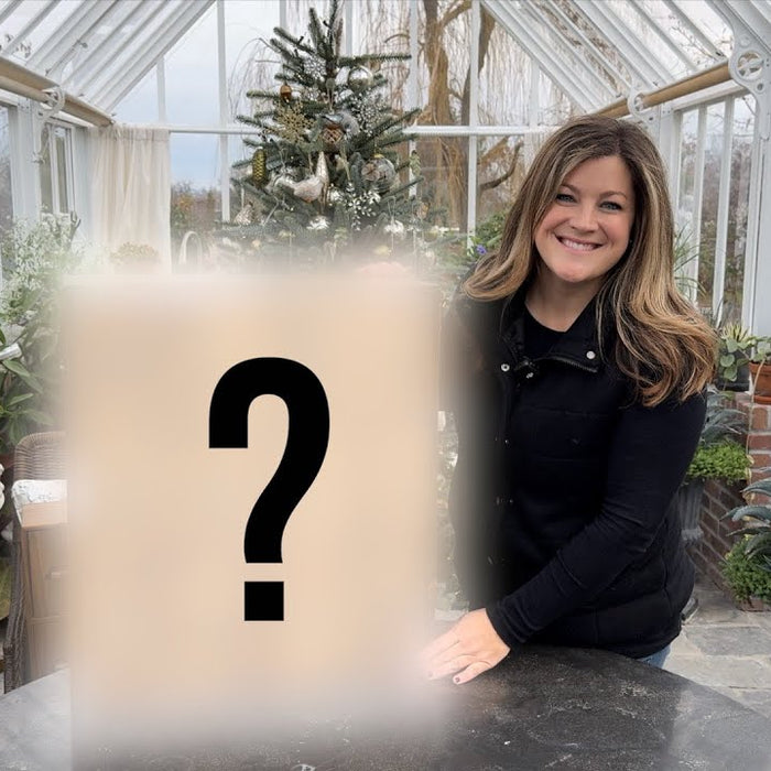 Laura in her green house holding a mysterious product with a ? sign