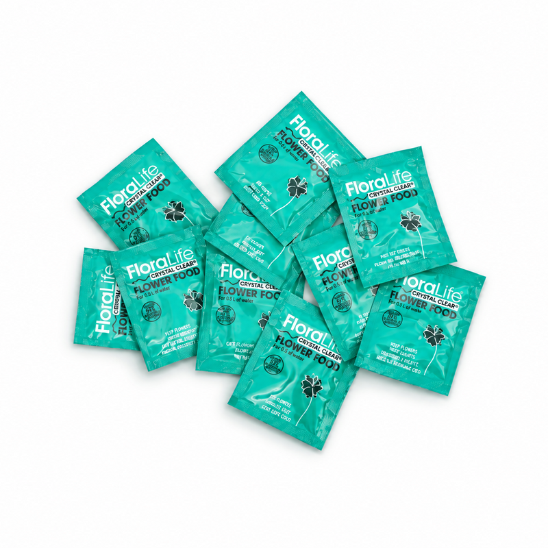 Ten green FloraLife Flower Food packets are arranged in a scattered pile on a white background. Designed as vase water conditioners, each packet features white text and a black flower icon on the front, helping to extend the life of your fresh arrangements.
