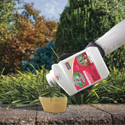 Person pouring a liquid from a labeled container into a small cap outdoors.
