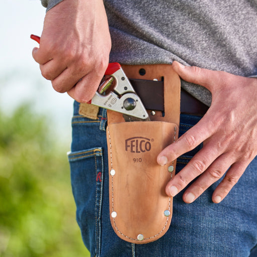 A person wearing a beige Felco 910 leather holster on their belt, holding a pruning shear inside it.