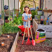 Child holding a red hoe, shovel, and rake
