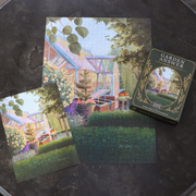 A completed Garden Answer puzzle titled "Golden Hour At The Greenhouse".  Its box, and a smaller image layout are arranged on a dark textured surface near.