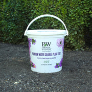 White bucket of Proven Winners Water Soluble plant food on a concrete surface with greenery in the background