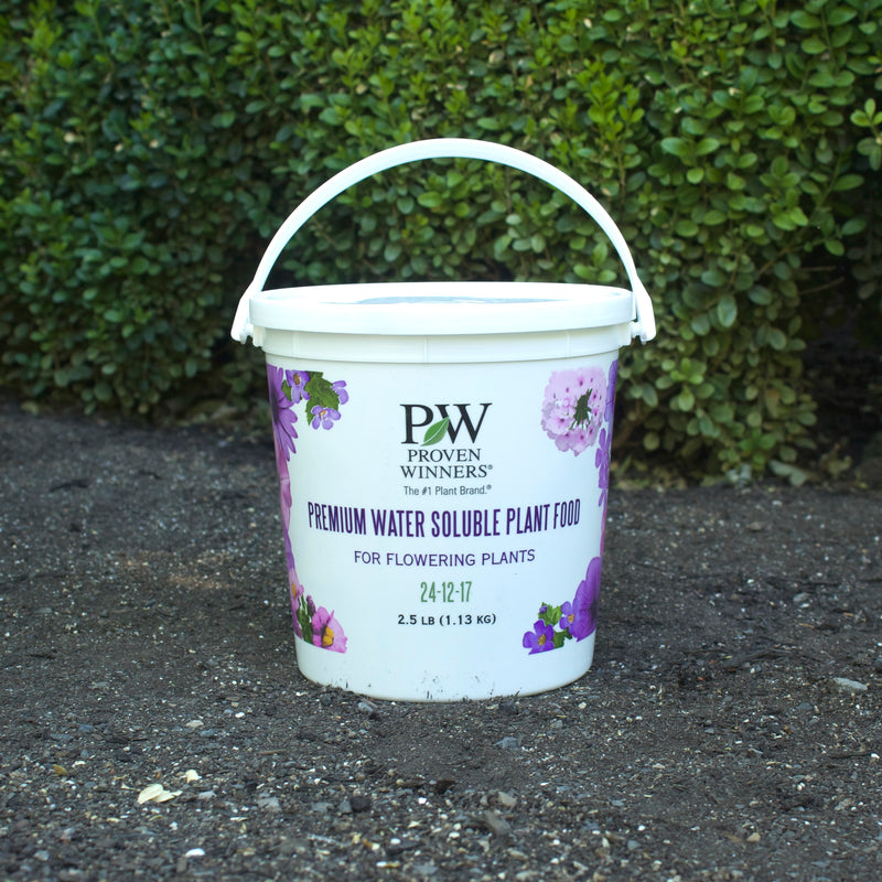 White bucket of Proven Winners Water Soluble plant food on a concrete surface with greenery in the background