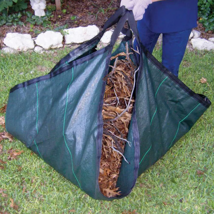 A person holds a DeWitt Leaf & Debris Tarp 9ft W x 9ft L filled with dry leaves and yard debris while standing on grass in a garden.