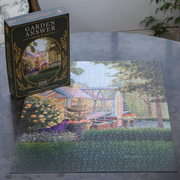 A completed 1000-piece jigsaw puzzle of a garden scene sits on a gray table next to its dark green 'Garden Answer' box.